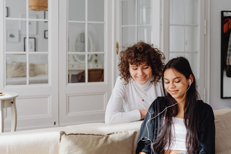Two friends sharing earphones on a sofa in a bright living room